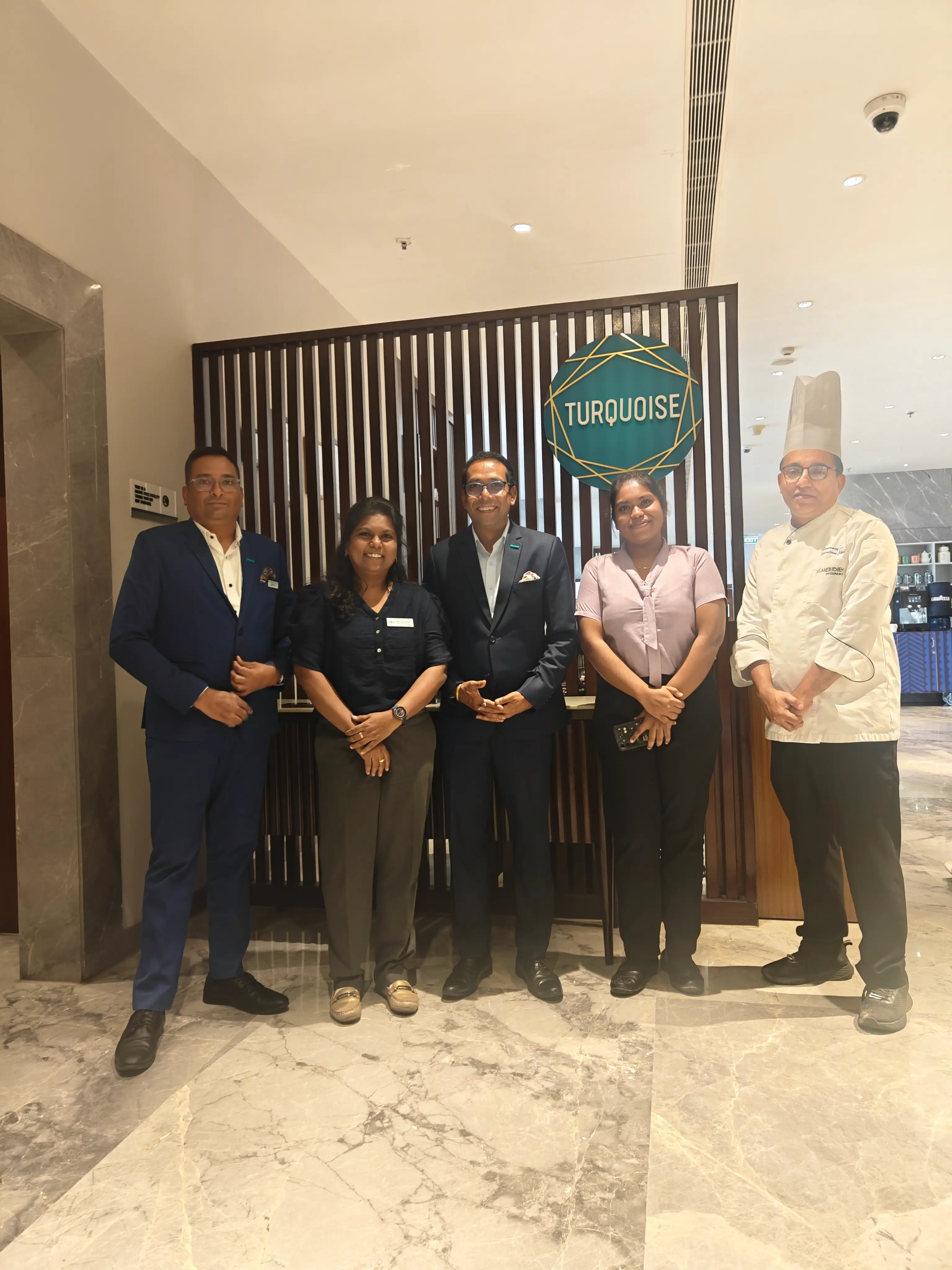 Hotel management team and a chef standing together in a hotel lobby.