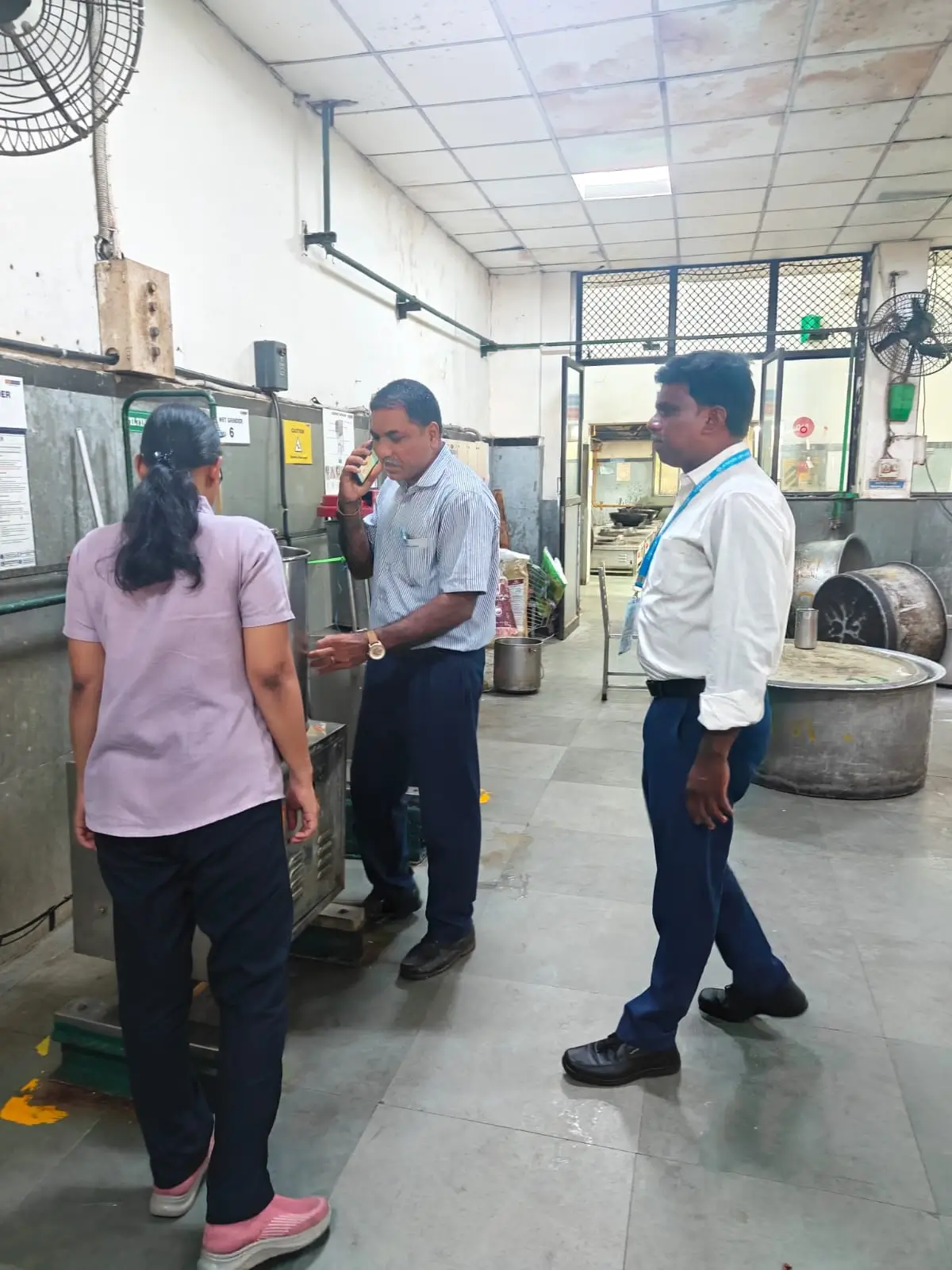 Two auditors walking through an industrial processing area discussing with an operator beside large machinery.