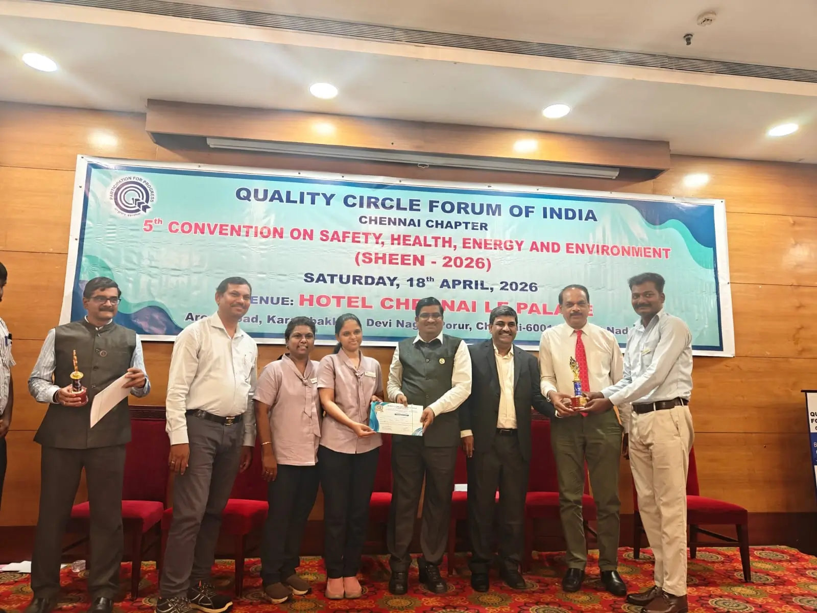 Participants receiving an award on stage in front of a banner for a quality, safety, health, energy and environment convention.